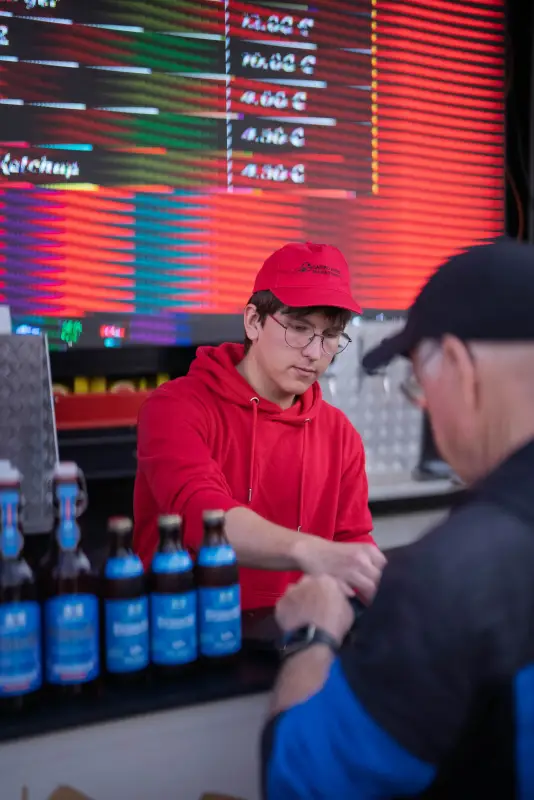 Servicekraft bedient einen Gast an der Theke vor der digitalen Preistafel